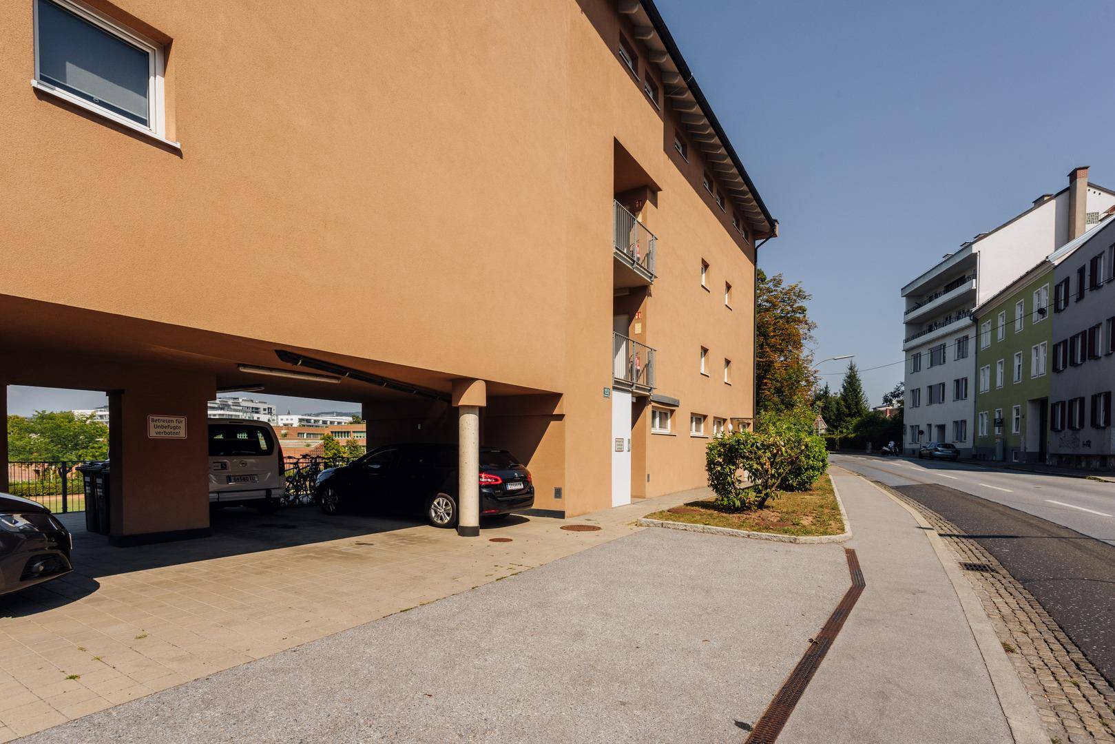 Seitenansicht des Gebäudes mit Carport, Parkplätzen und Zugang zur Straße.