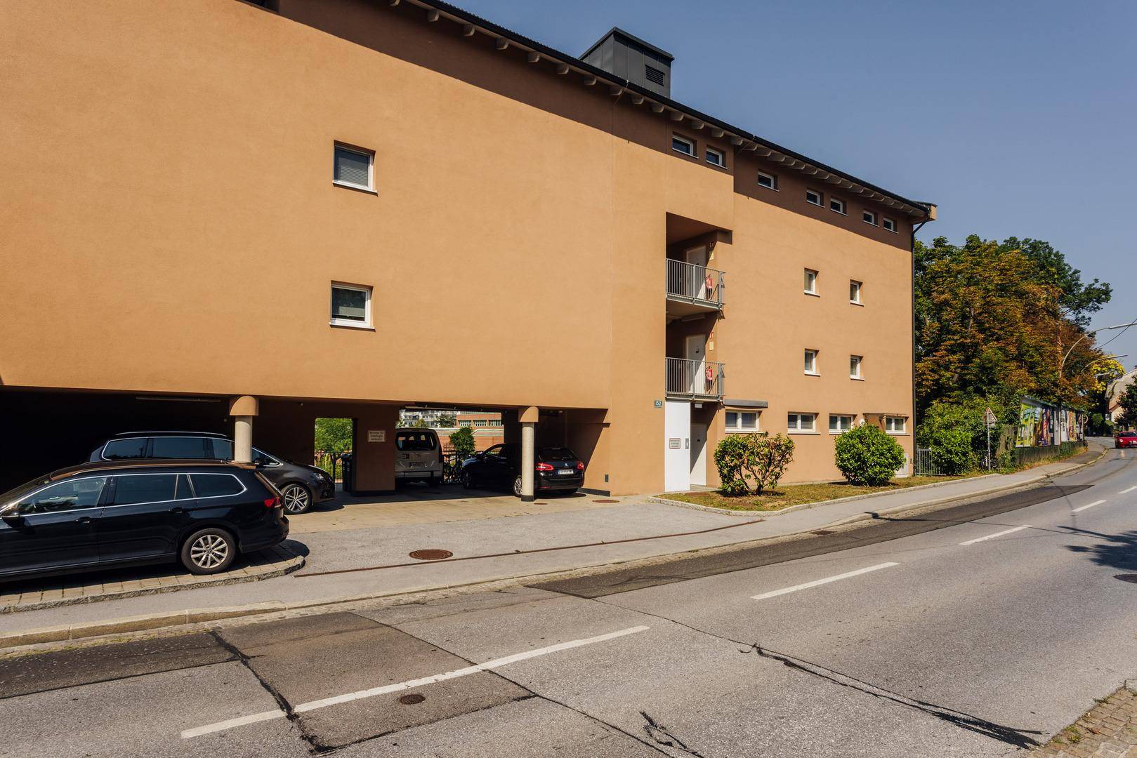 Ansicht des modernen Gebäudes von der Straße mit Parkplätzen und Carport.