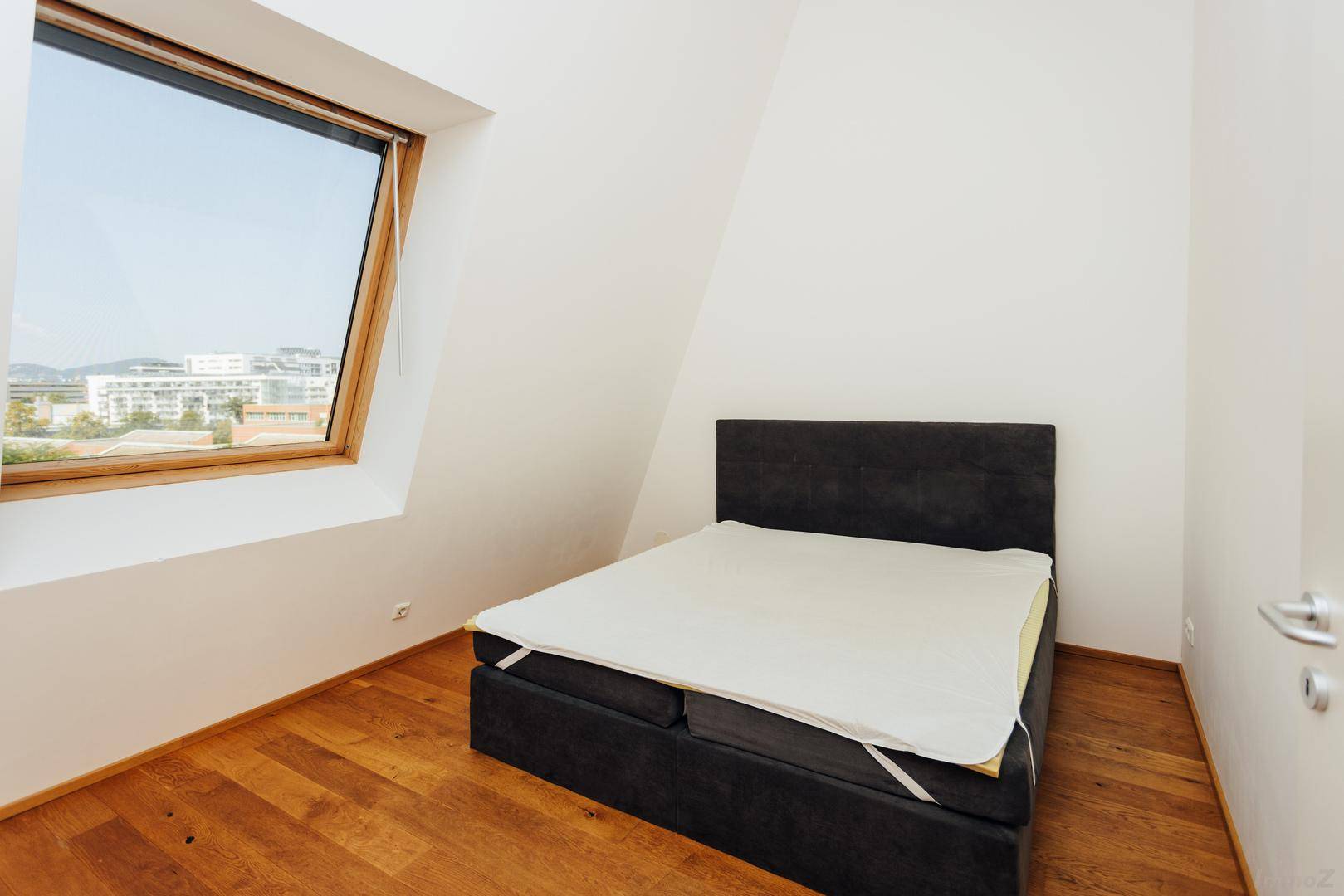 Geräumiges Schlafzimmer im Dachgeschoss mit Holzboden, Dachfenster und Blick auf die Stadt.