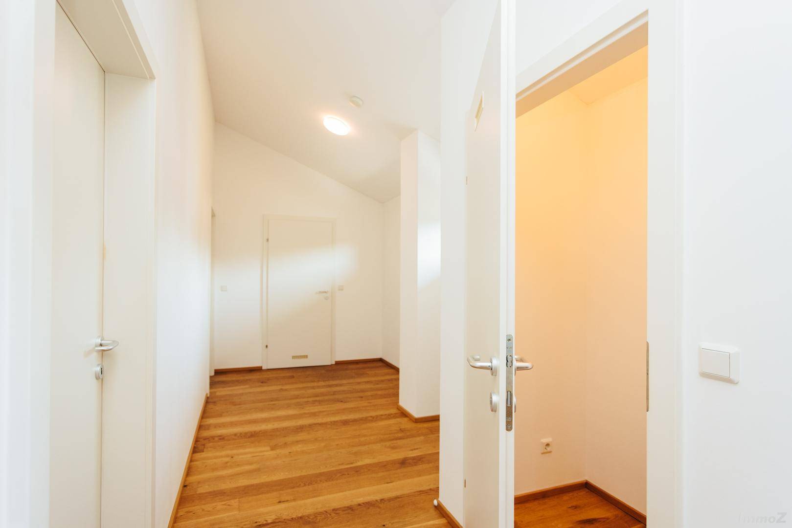 Heller Flur mit Holzboden, mehreren Türen und Dachschrägen.