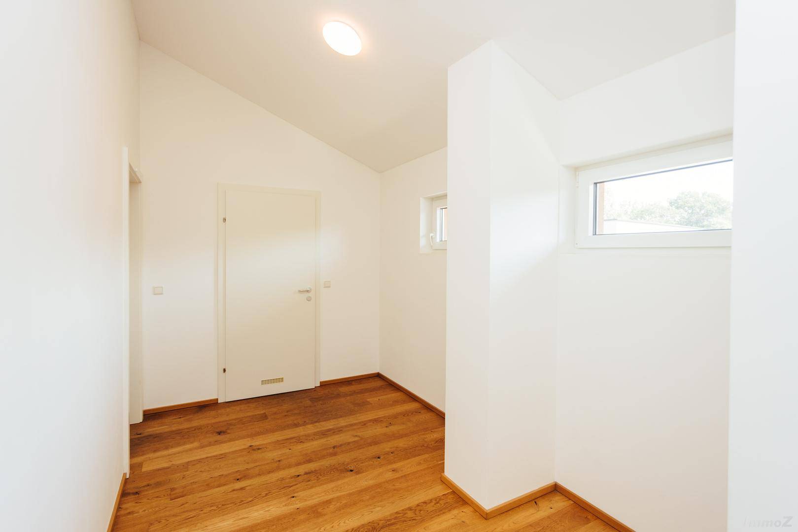 Heller Flur mit Holzboden, weißen Wänden und schrägen Decken im Dachgeschoss.