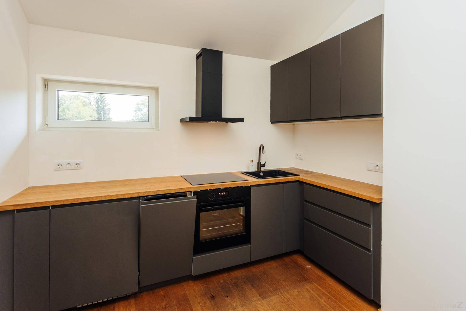 Moderne Küche mit dunklen Schränken, Holzarbeitsplatte, Induktionskochfeld und Fenster.