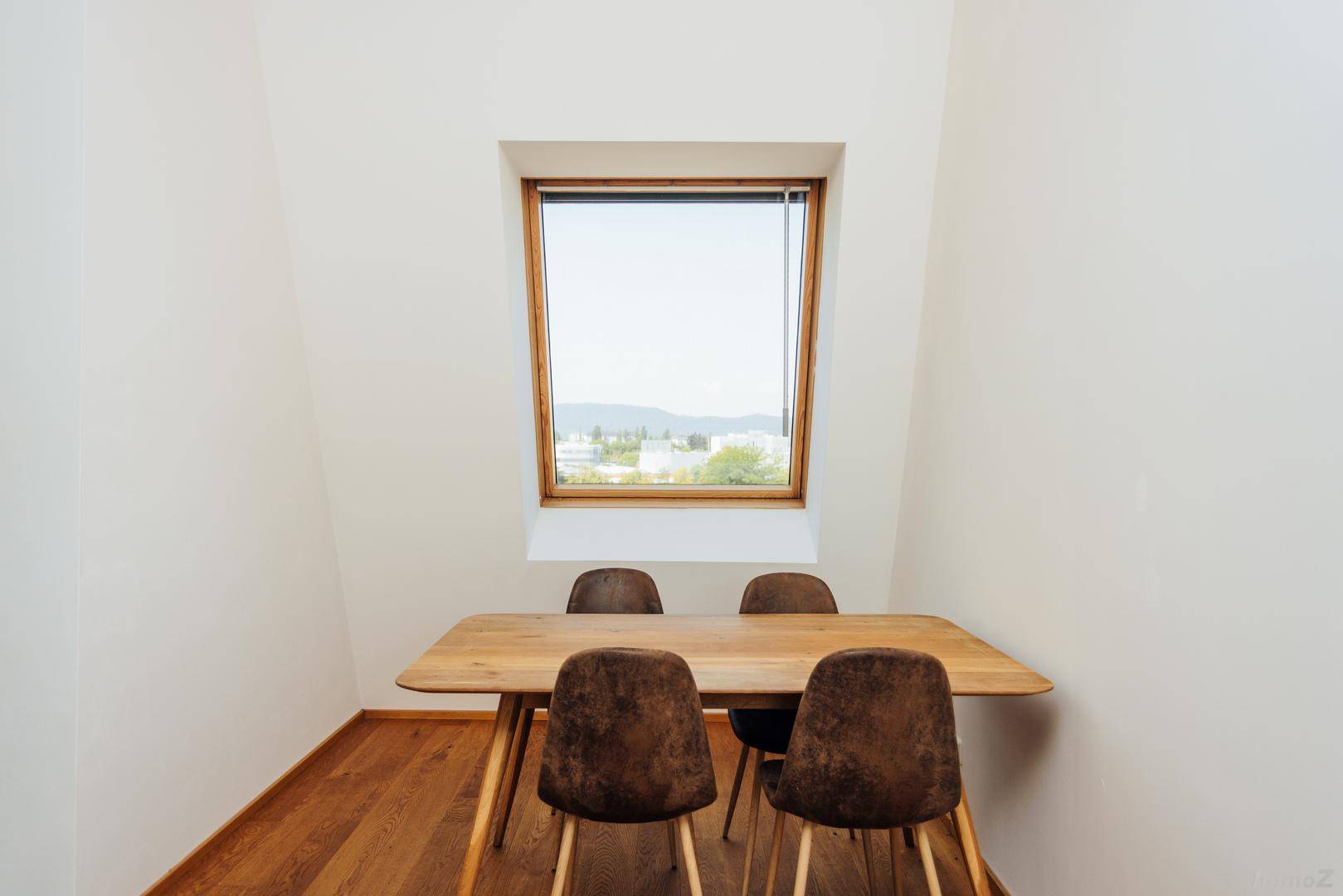 Heller Essbereich mit Holztisch, modernen Stühlen und einem Dachfenster mit Bergblick.