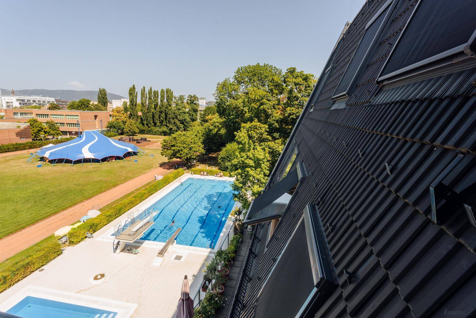 Panoramablick auf das Schwimmbad, Sportanlagen und das Dach des Gebäudes mit Dachfenstern.