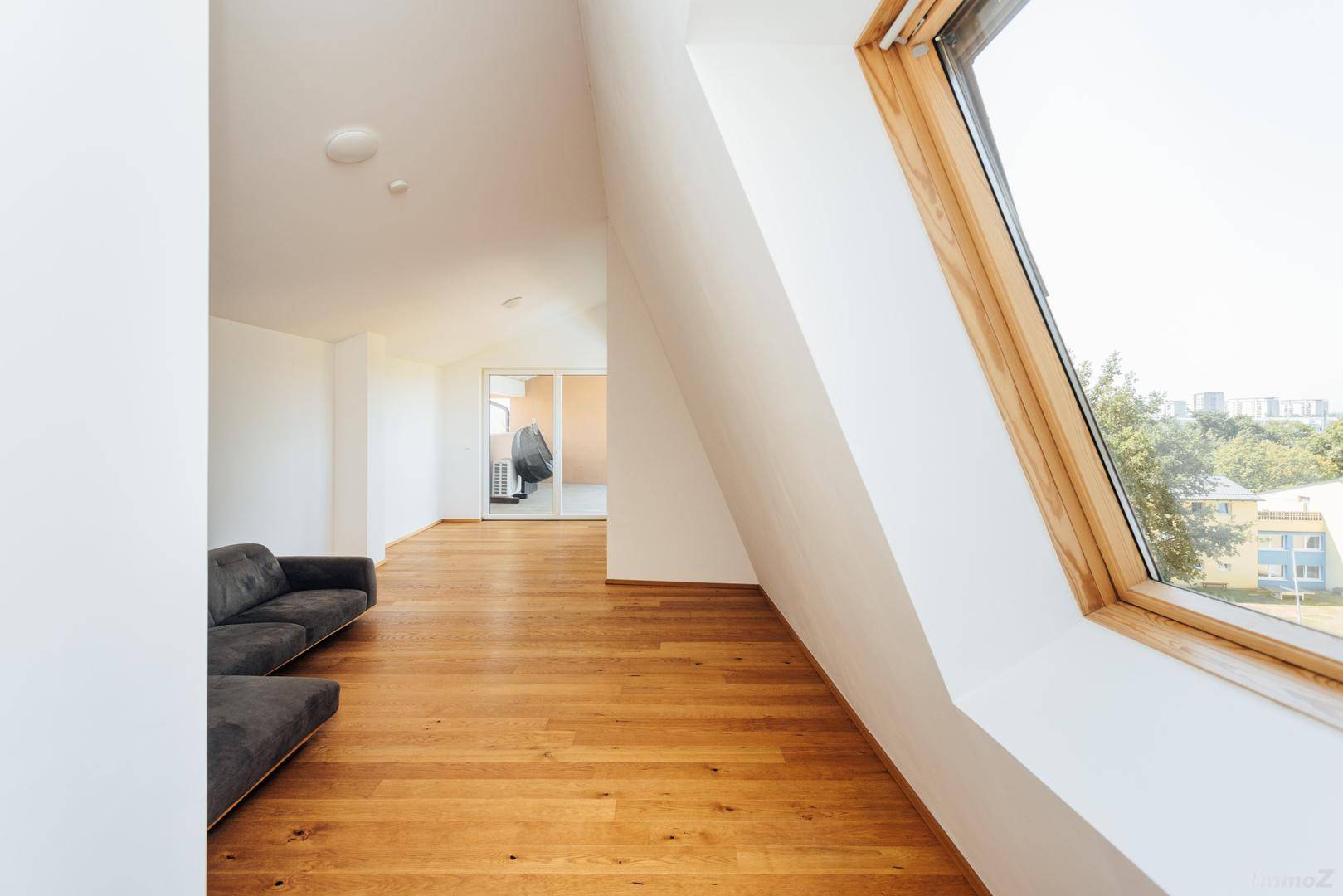 Helles Wohnzimmer mit Holzboden, Dachschrägen und einem großen Dachfenster mit Ausblick.