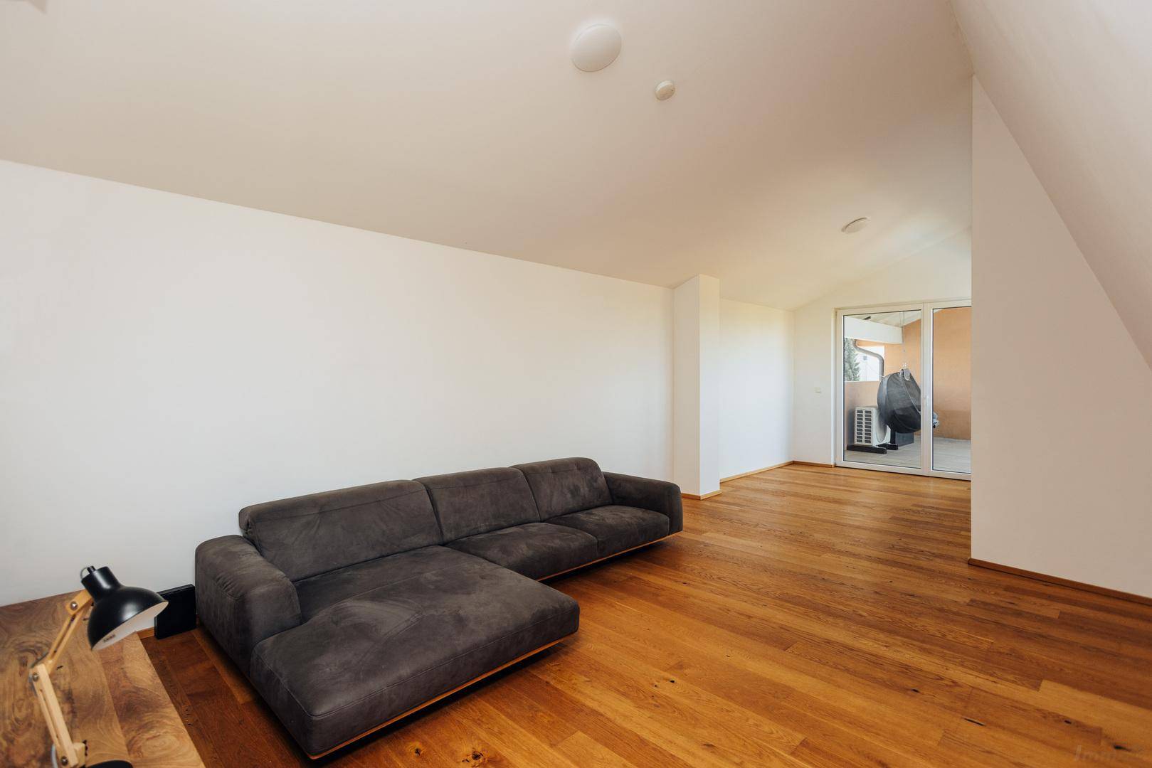 Geräumiges Wohnzimmer mit Holzboden, Dachschrägen und direktem Zugang zum Balkon.