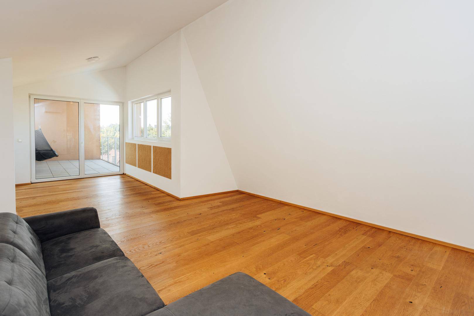 Lichtdurchflutetes Wohnzimmer mit Holzboden, Schiebetür zum Balkon und großen Fenstern.