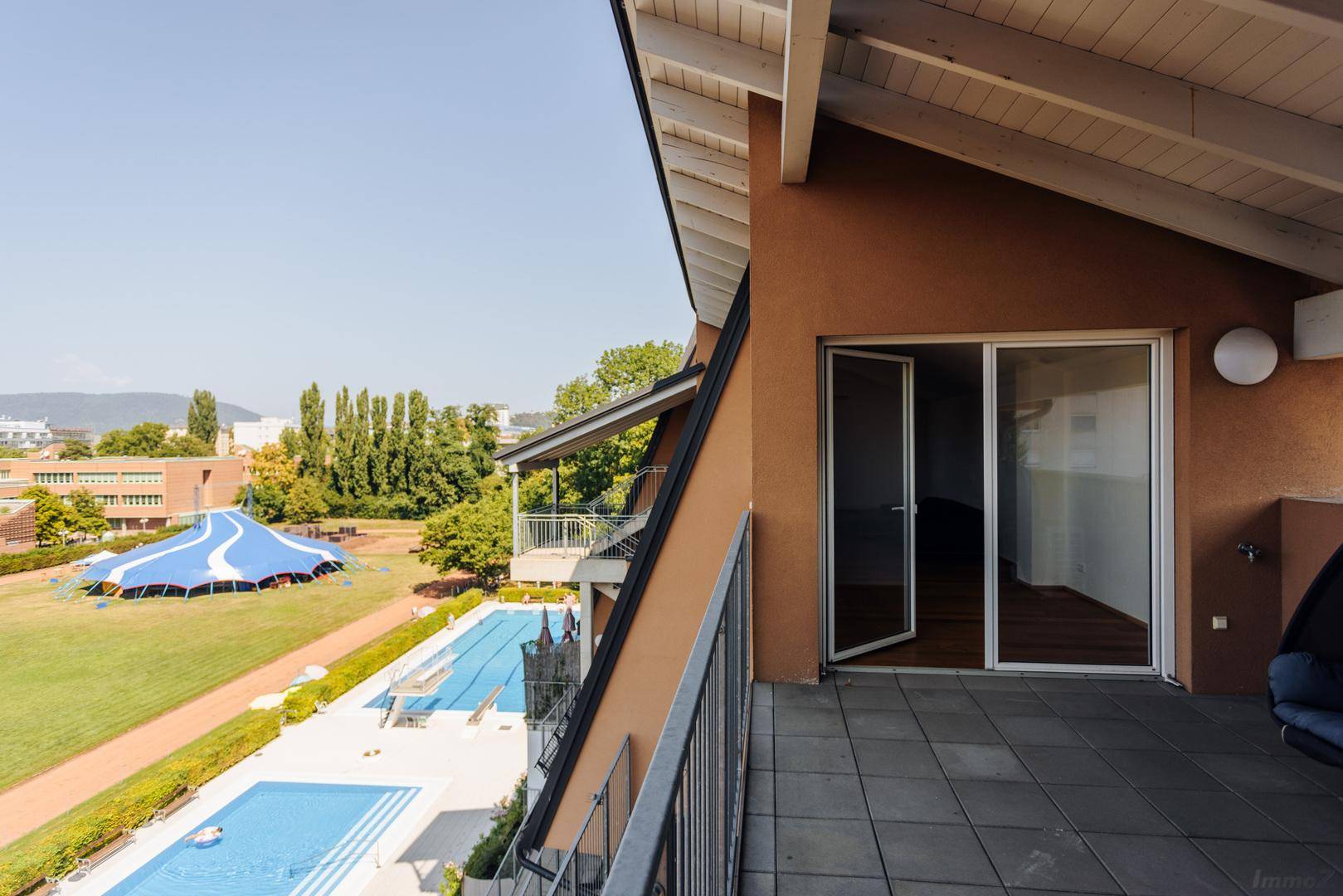 Großer Balkon mit Poolblick, grüner Umgebung und freiliegenden Holzbalken.