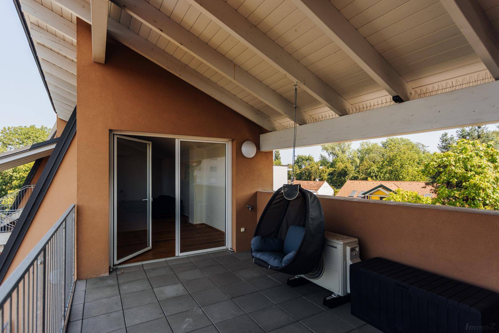 Geräumiger Balkon mit Fliesenboden, Hängesessel und freiliegenden Holzbalken.