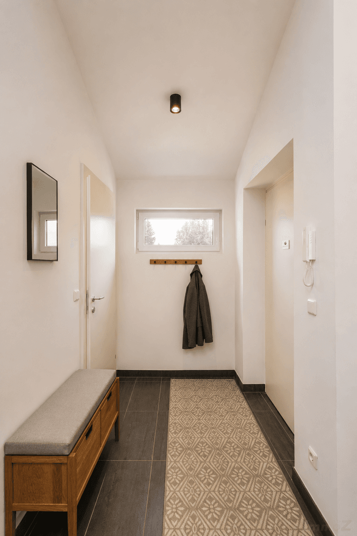 Heller Flur mit gepolsterter Sitzbank, Garderobe und einem dekorativen Teppichläufer.