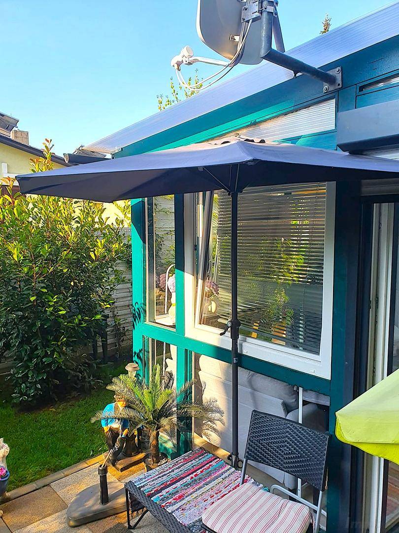 Außenbereich mit Terrasse, Sonnenschirm und Blick auf den grünen Garten.