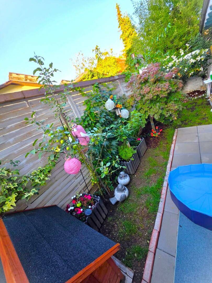 Kleiner, gepflegter Gartenbereich mit Obstbaum, Blumenbeeten und Holzzaun.