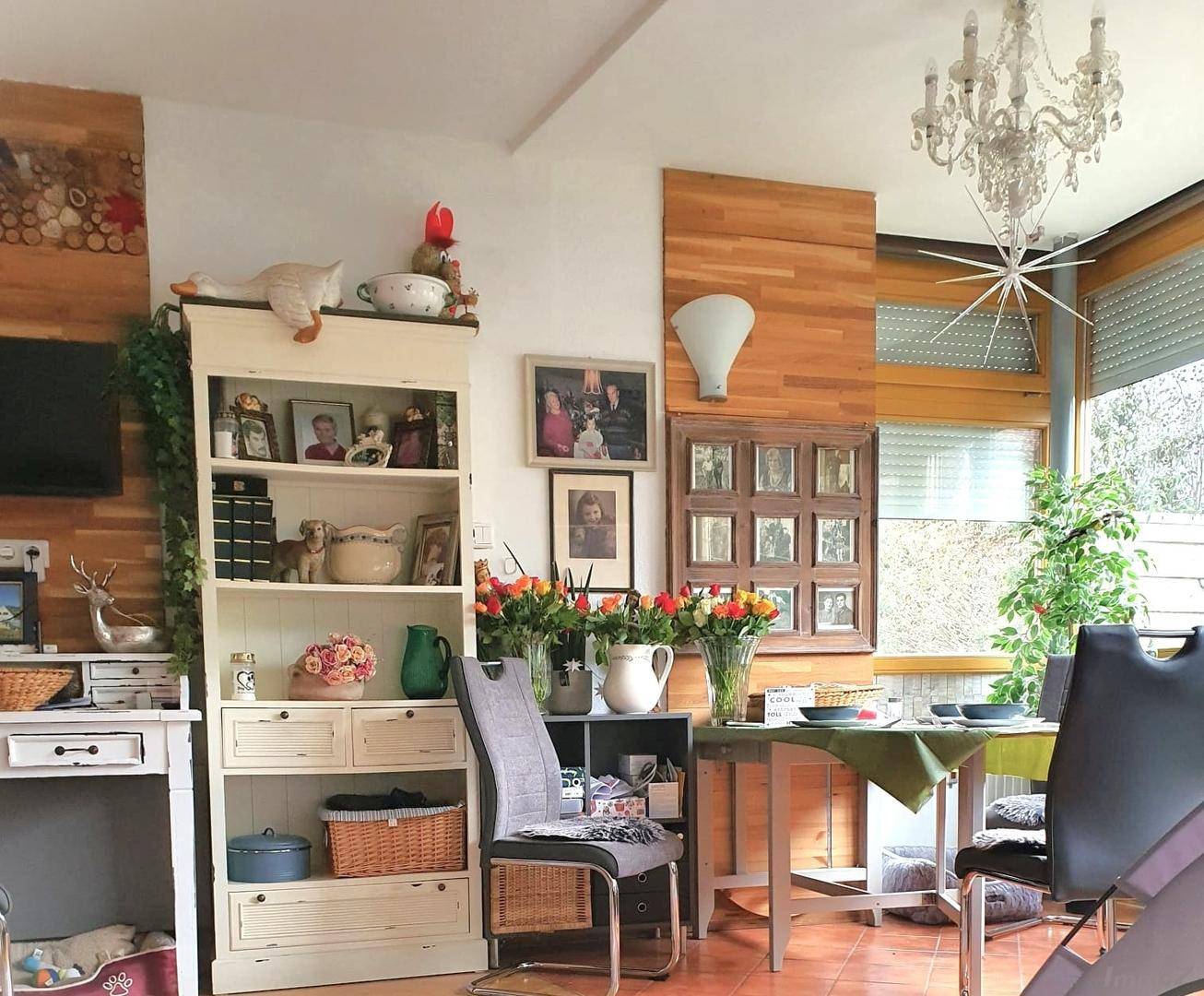 Gemütlicher Wohn-Essbereich mit Kronleuchter, Holzelementen und Blick in den Garten.