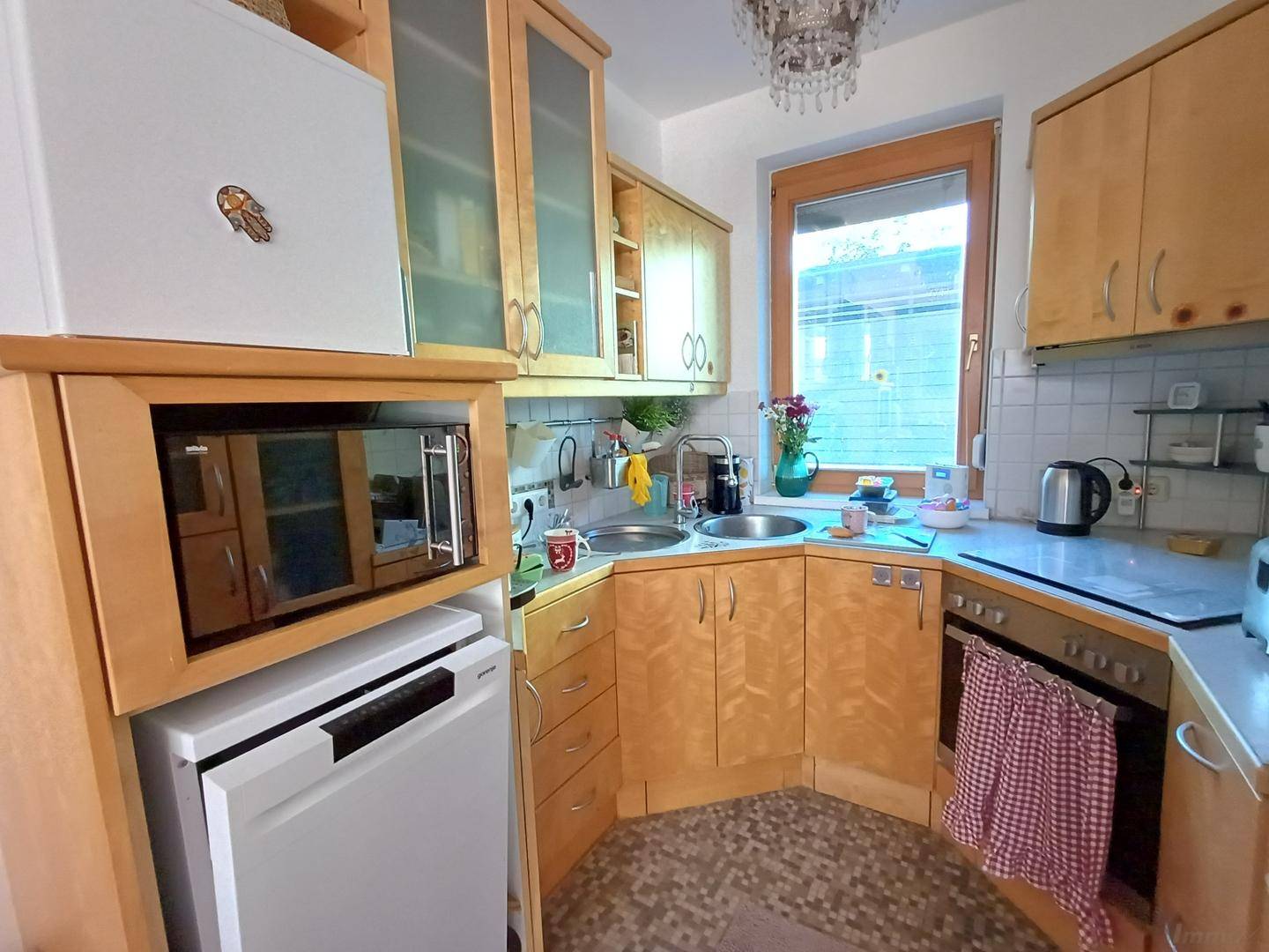 Kleine, funktionale Küche mit Holzschränken, Einbaugeräten und Fenster.