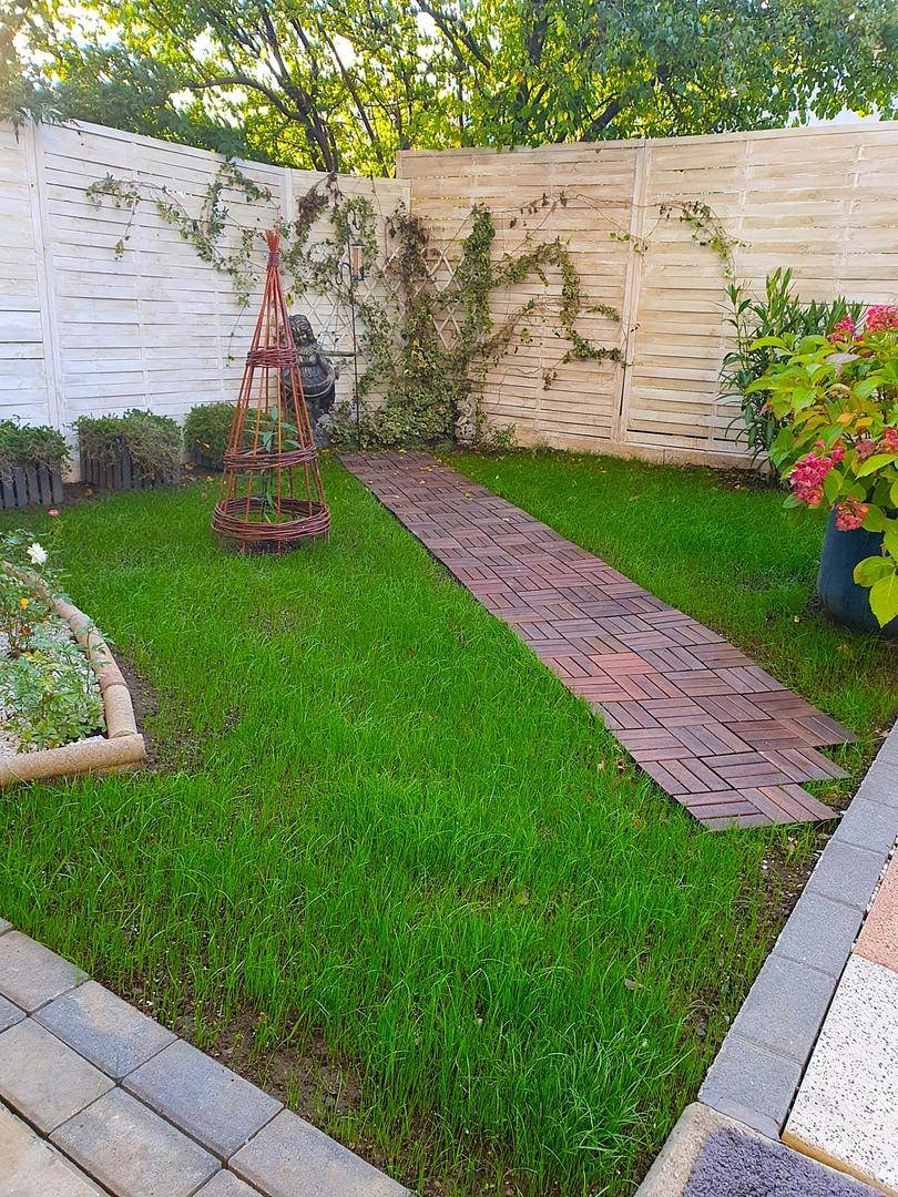 Gepflegter Gartenbereich mit Rasenfläche, Holzweg und dekorativem Zaun.