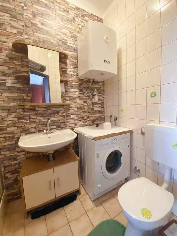 Badezimmer mit Waschbecken, Toilette, Waschmaschine und Wandfliesen in Steinoptik.