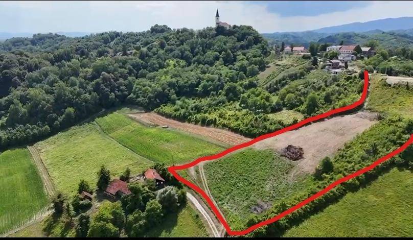 Luftaufnahme eines Grundstücks mit roter Markierung, umgeben von grünen Feldern und einem Dorf mit Kirche auf einem Hügel.