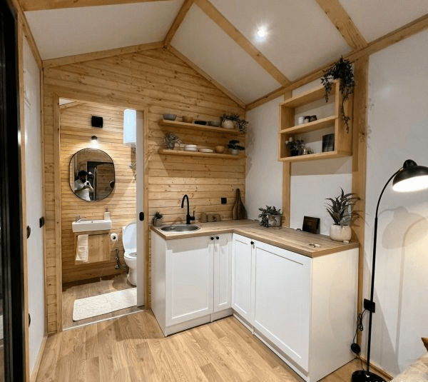 Gemütliche Küchenzeile in einem Holzhaus mit hellem Interieur und Zugang zu einem kleinen Badezimmer.