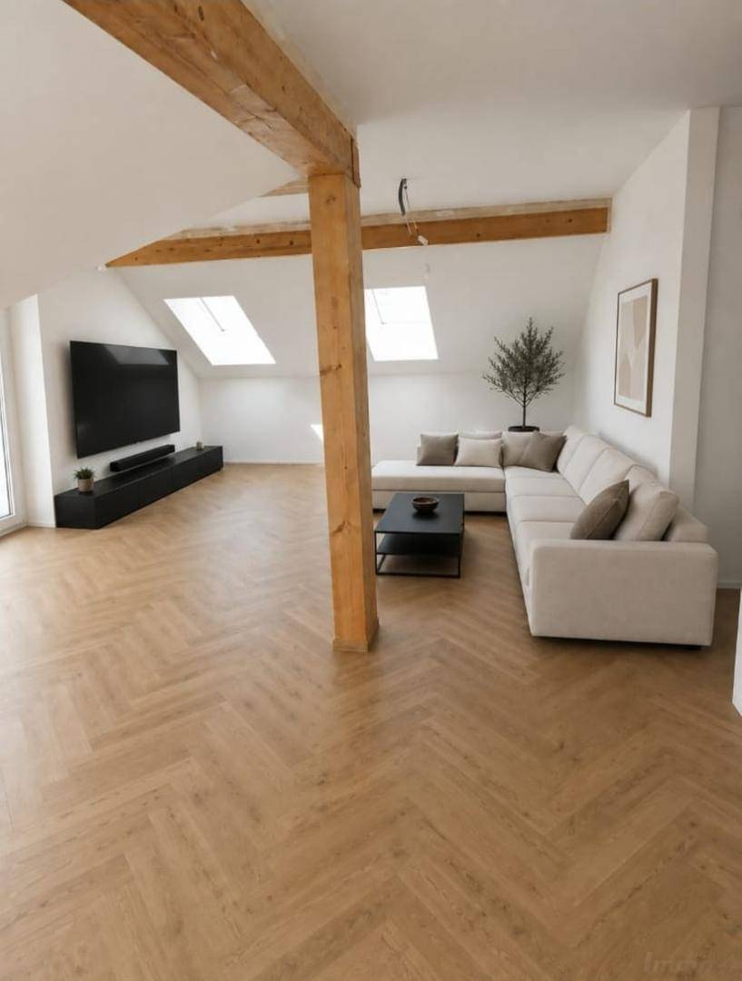 Helles Wohnzimmer im Dachgeschoss mit sichtbaren Holzbalken, gemütlichem Sofa und großen Dachfenstern.