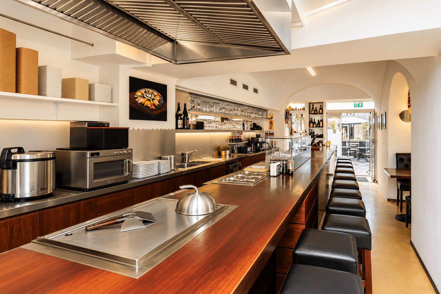 Professionelle Restaurantküche mit langer Holztheke, Edelstahlflächen und Dunstabzugshaube.