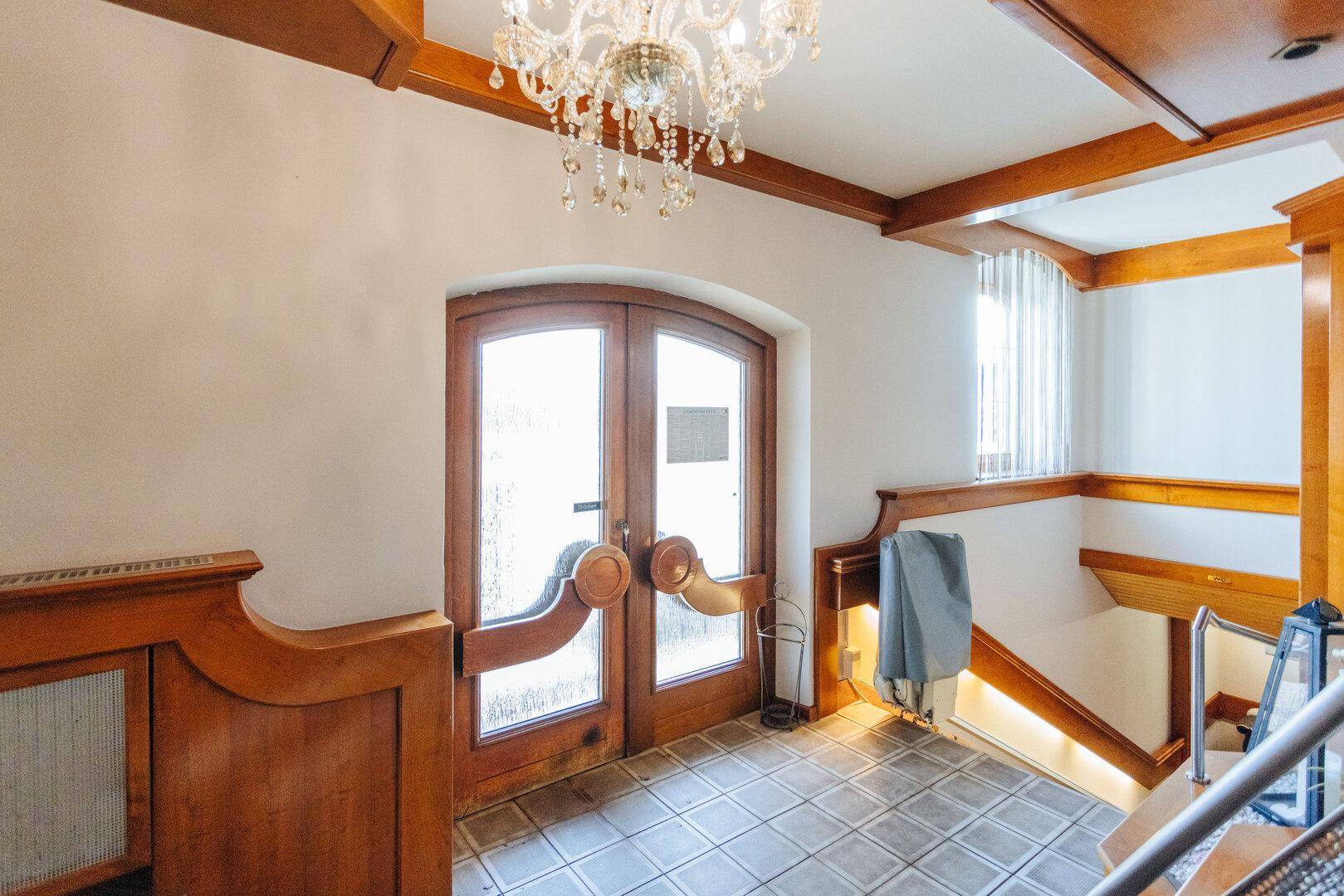 Eingangsbereich mit rustikalen Holztüren, gefliestem Boden und einer eleganten Kristallleuchte an der Decke.