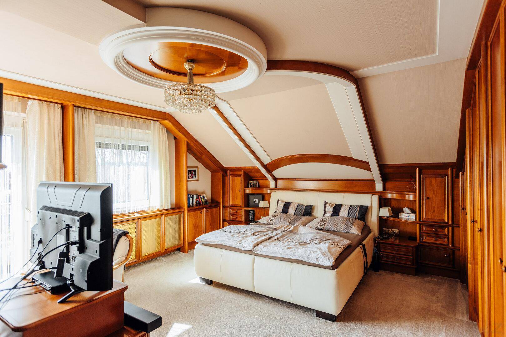 Geräumiges Schlafzimmer im Dachgeschoss mit schrägen Decken, Einbauschränken aus Holz und einem großen Bett.