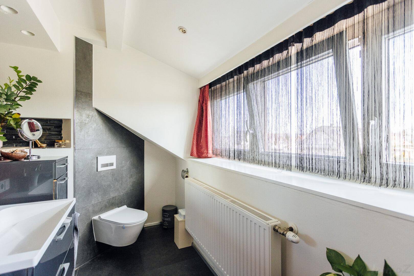 Modernes Badezimmer im Dachgeschoss mit wandhängendem WC, dunklen Fliesen und einem Fenster.