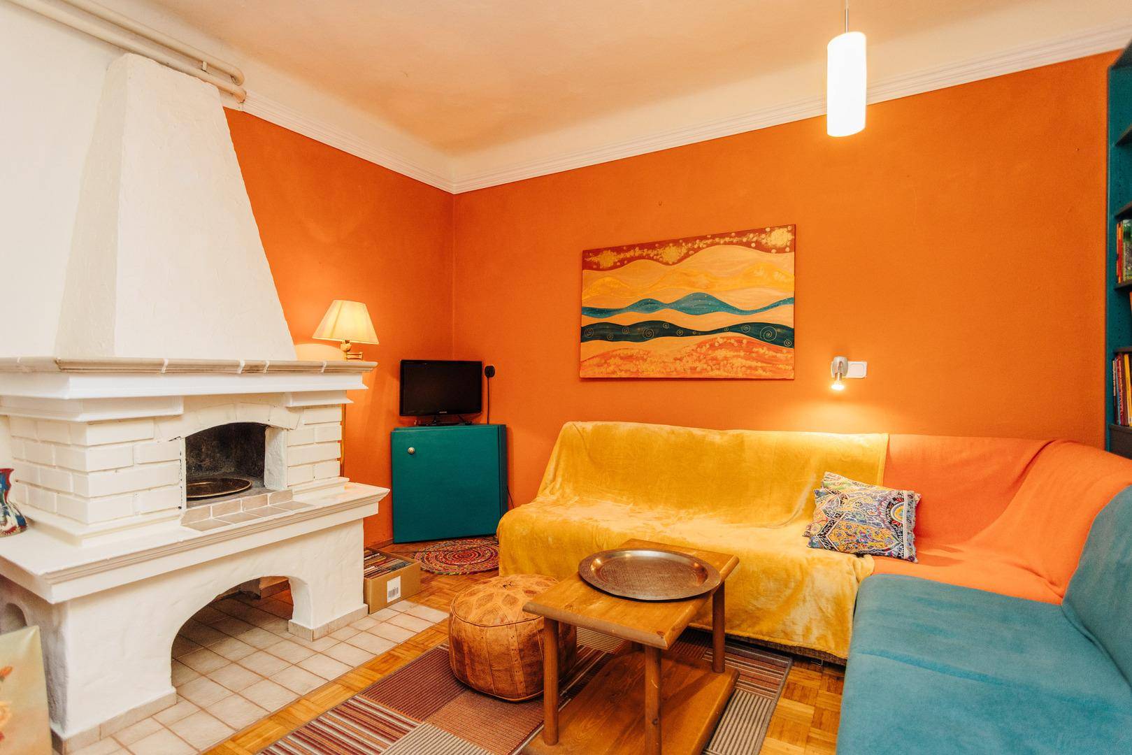 Gemütliches Wohnzimmer mit Kamin, orangefarbenen Wänden und farbenfrohen Sofas.