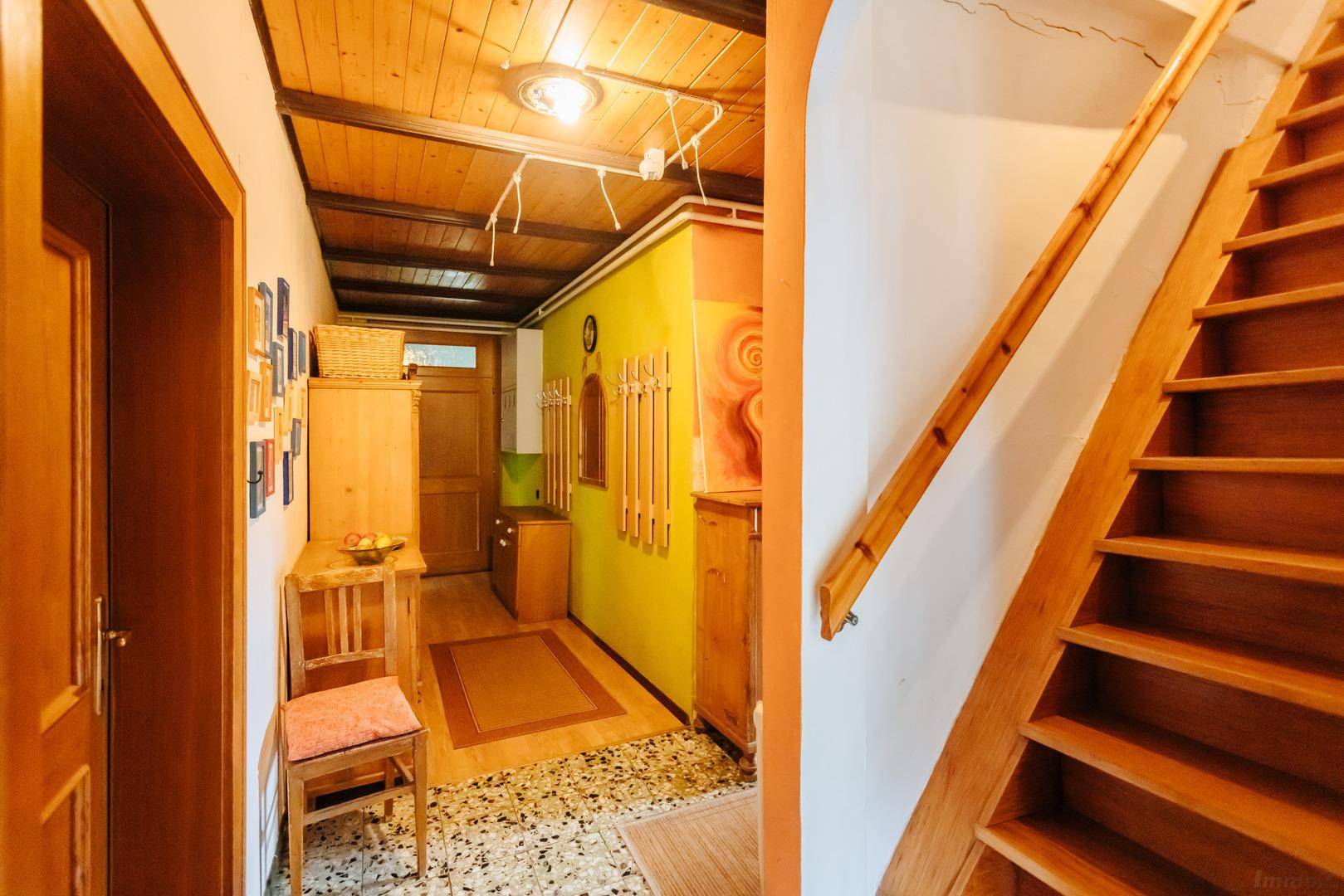 Heller Flur mit Holztreppe, farbenfrohen Wänden und einer rustikalen Holzdecke.