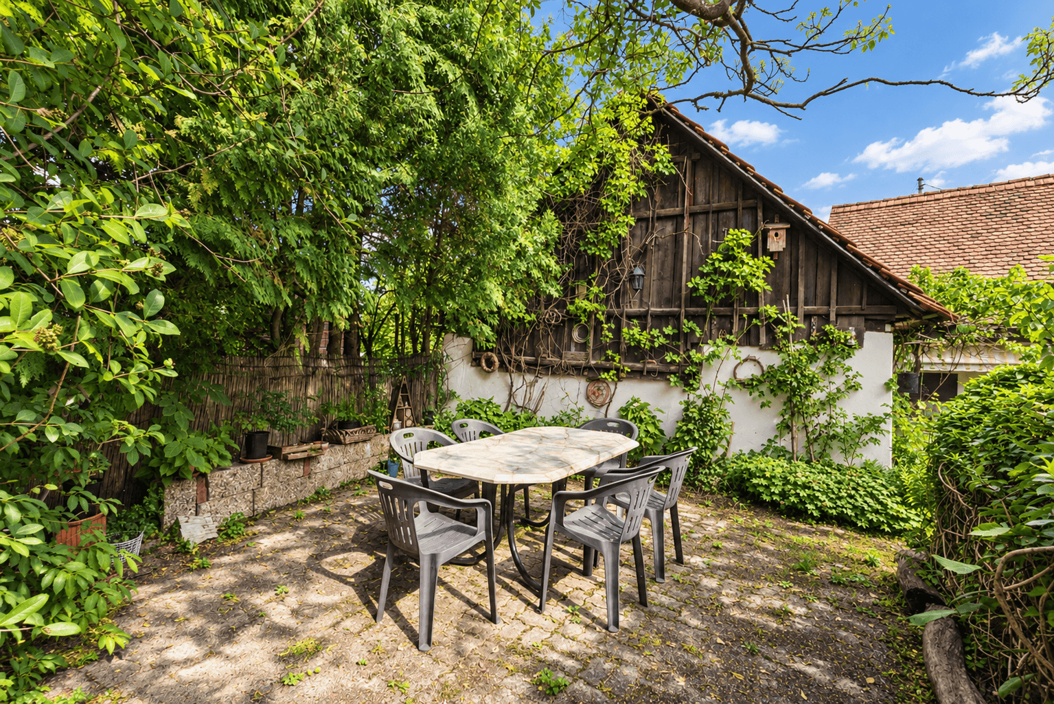 Gemütlicher Essbereich im Freien mit Tisch und Stühlen, neben einem rustikalen Holzgebäude im Garten.