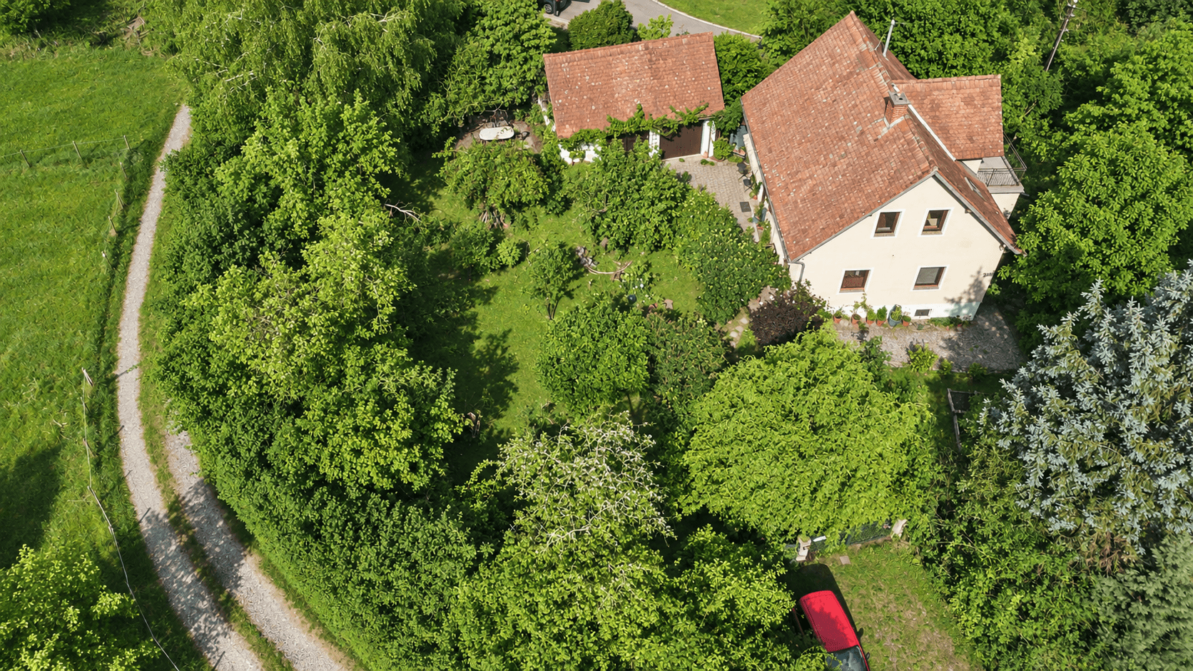Luftaufnahme des Anwesens mit Haupthaus, Nebengebäude, weitläufigem Garten und einem Feldweg.