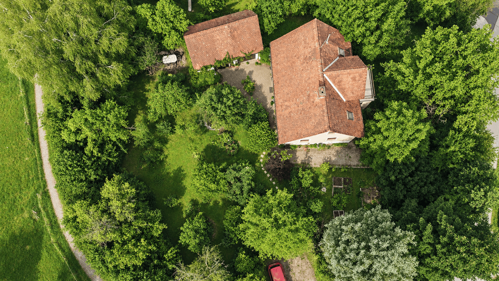 Draufsicht auf das Anwesen mit Haupthaus, Nebengebäude, Garten und einem geschwungenen Weg.