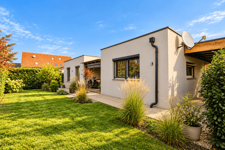 Moderne Hausfassade mit großen Fenstern, Rollläden und gepflegtem Gartenbereich.