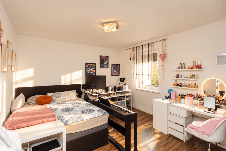 Jugendzimmer mit Bett, Schreibtisch, Klavier und Fenster für natürliches Licht.