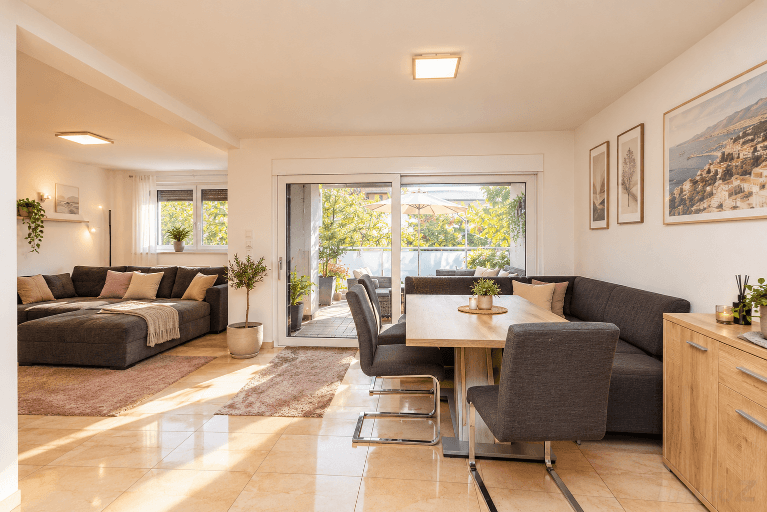 Heller Wohn- und Essbereich mit Fliesenboden und Zugang zu einem möblierten Balkon.