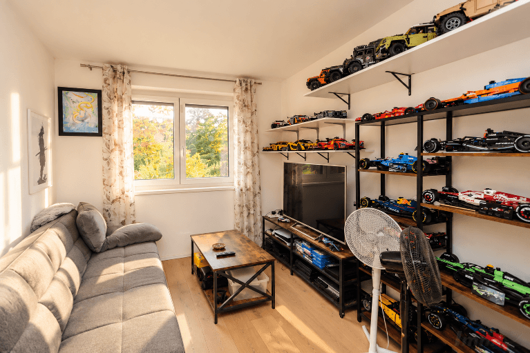 Hobbyraum mit Sofa, Fernseher und Regalen voller Modellautos, hell und freundlich.