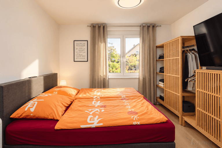 Schlafzimmer mit Doppelbett, Holzregal und Fenster mit Blick ins Grüne.