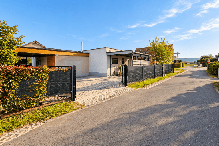Zufahrt zum modernen Einfamilienhaus mit Zaun und gepflastertem Vorplatz.