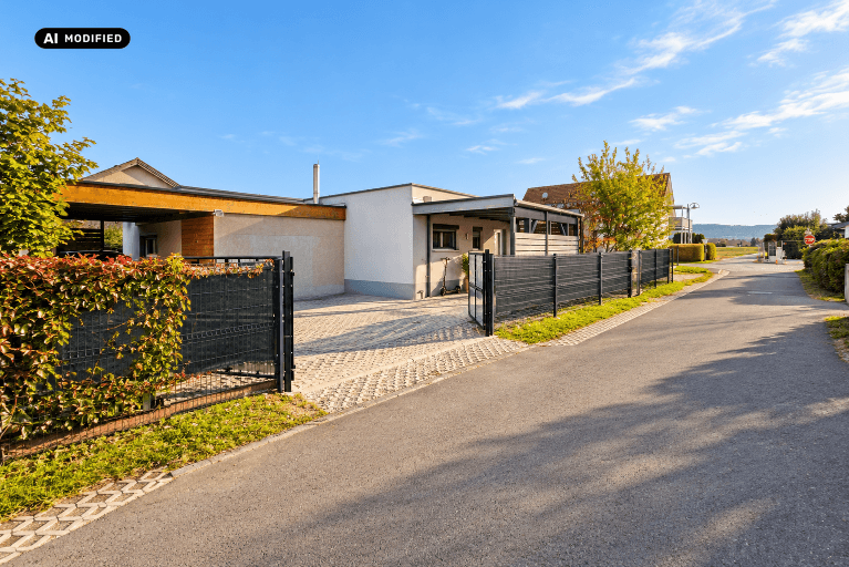 Zufahrt zum modernen Haus mit gepflastertem Hof, Zaun und Carport im Hintergrund.