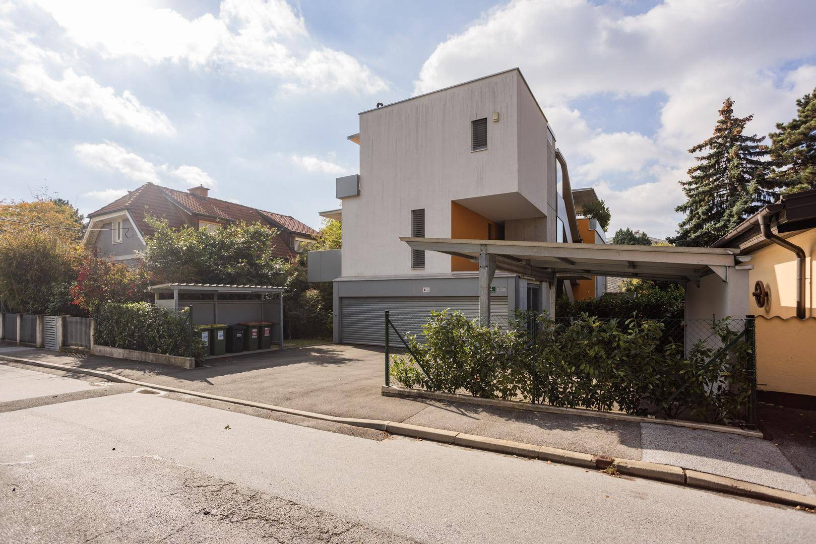 Ansicht des modernen Wohngebäudes von der Straße mit Carports und gepflegter Außenanlage.