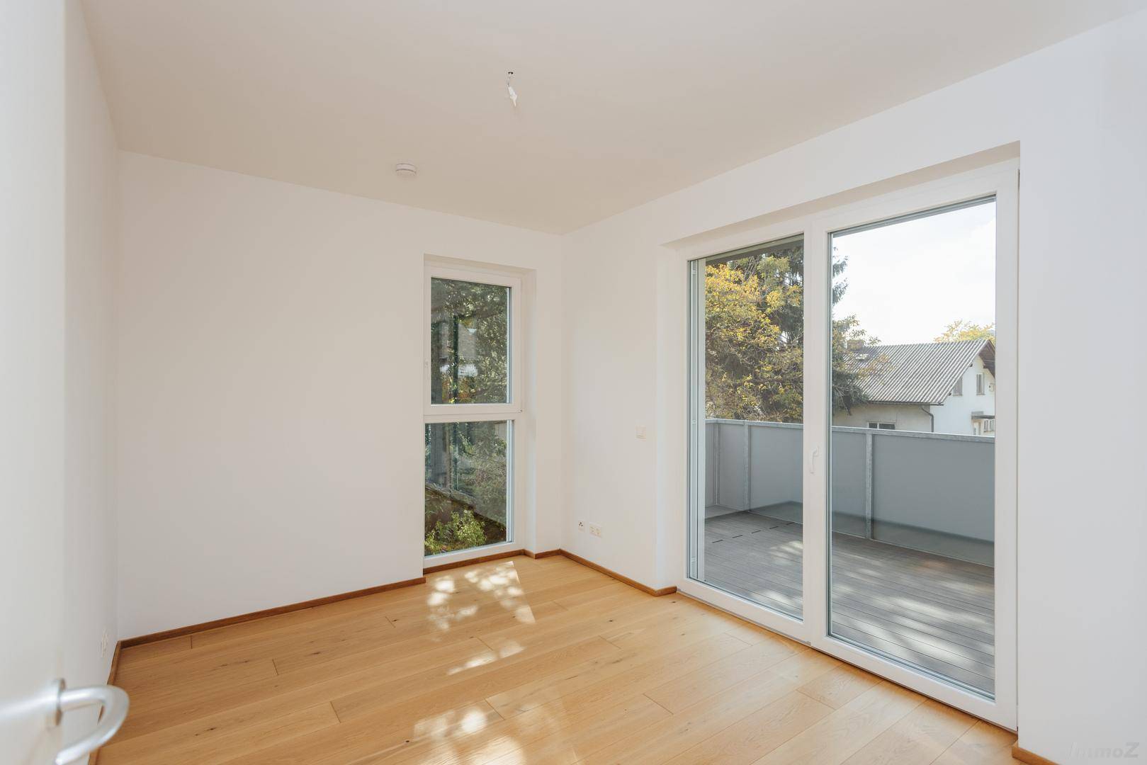 Heller, leerer Raum mit Holzboden und Zugang zu einem Balkon durch große Schiebetüren.