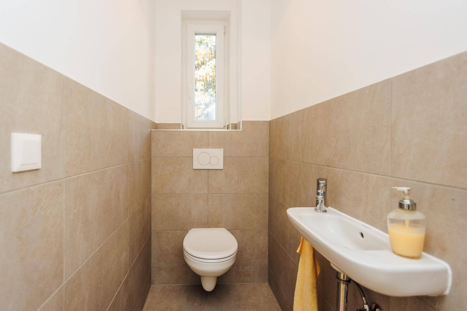 Helles Gäste-WC mit wandhängender Toilette und kleinem Handwaschbecken.