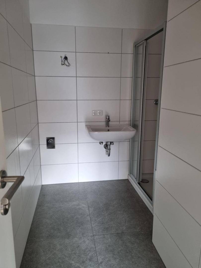 Modernes Badezimmer mit weißen Wandfliesen, grauen Bodenfliesen, einem Waschbecken und einer Duschkabine.