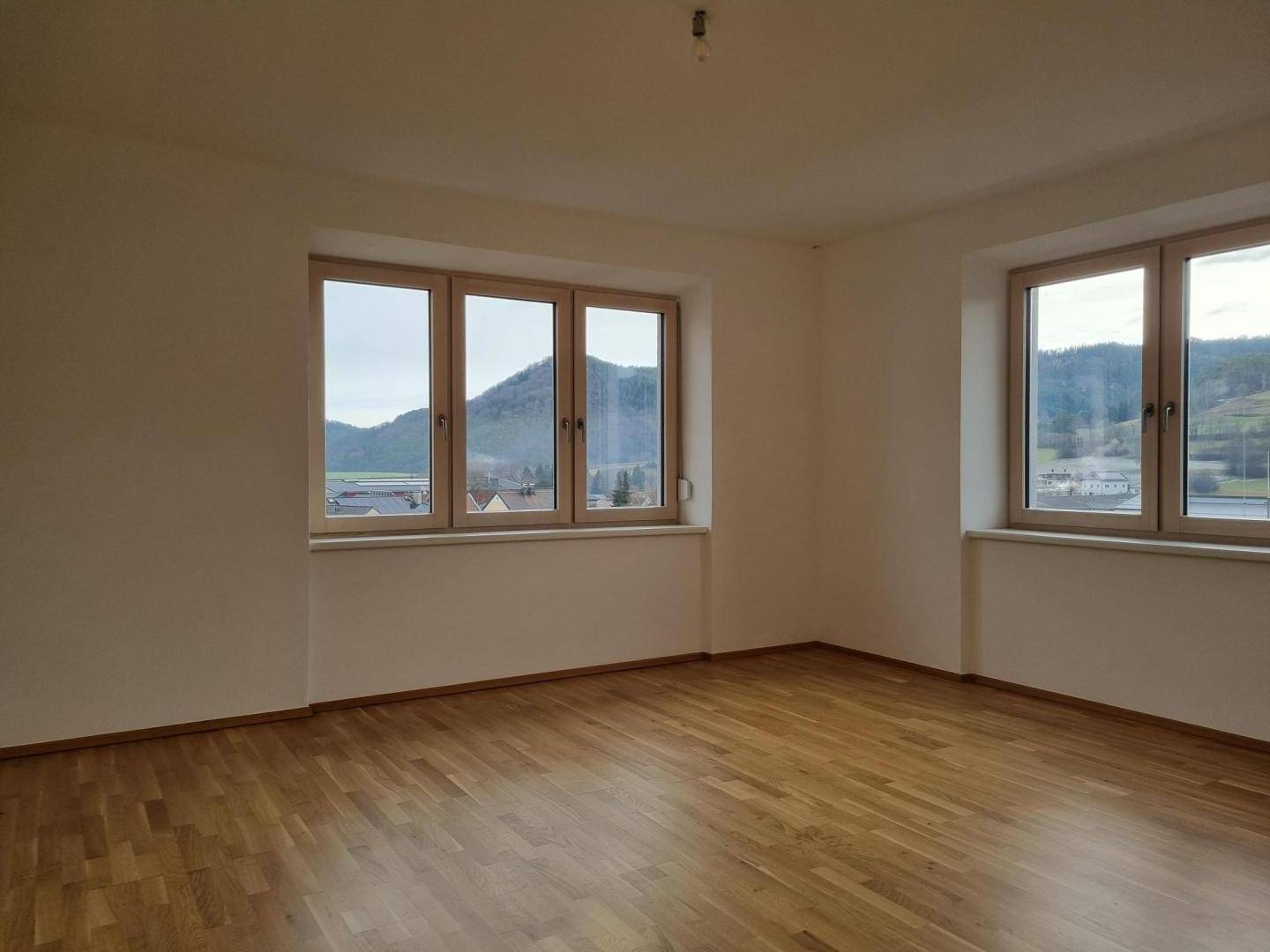 Geräumiger Raum mit Parkettboden und großen Fenstern, die einen weiten Blick auf die Berge bieten.