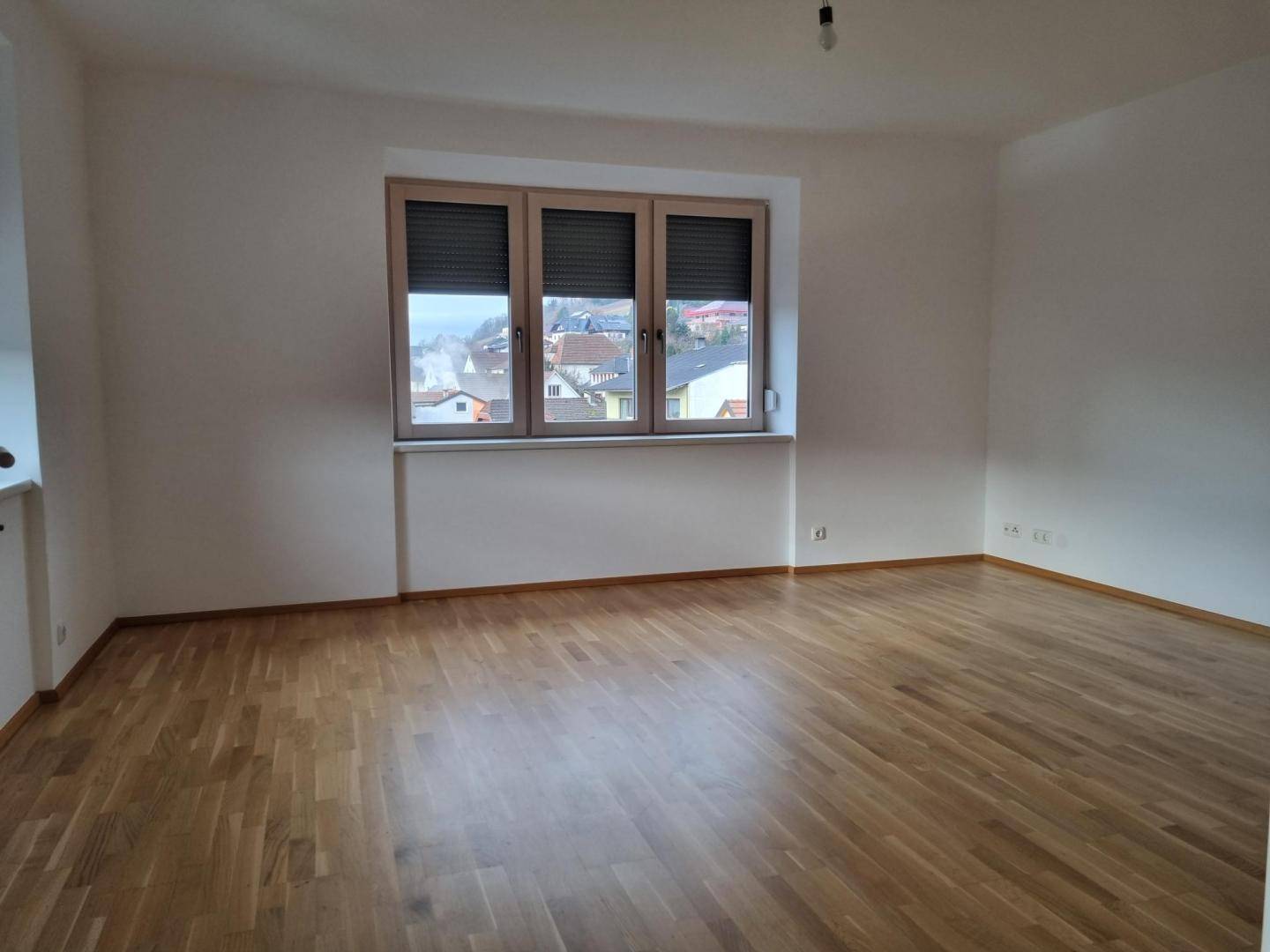 Heller Raum mit Parkettboden und Fenster mit Blick auf die umliegende Wohngegend und Hügel.