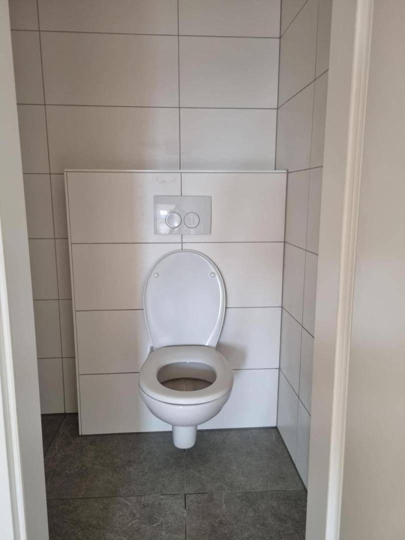 Separates WC mit wandmontierter Toilette und modernen Fliesen an Wänden und Boden.