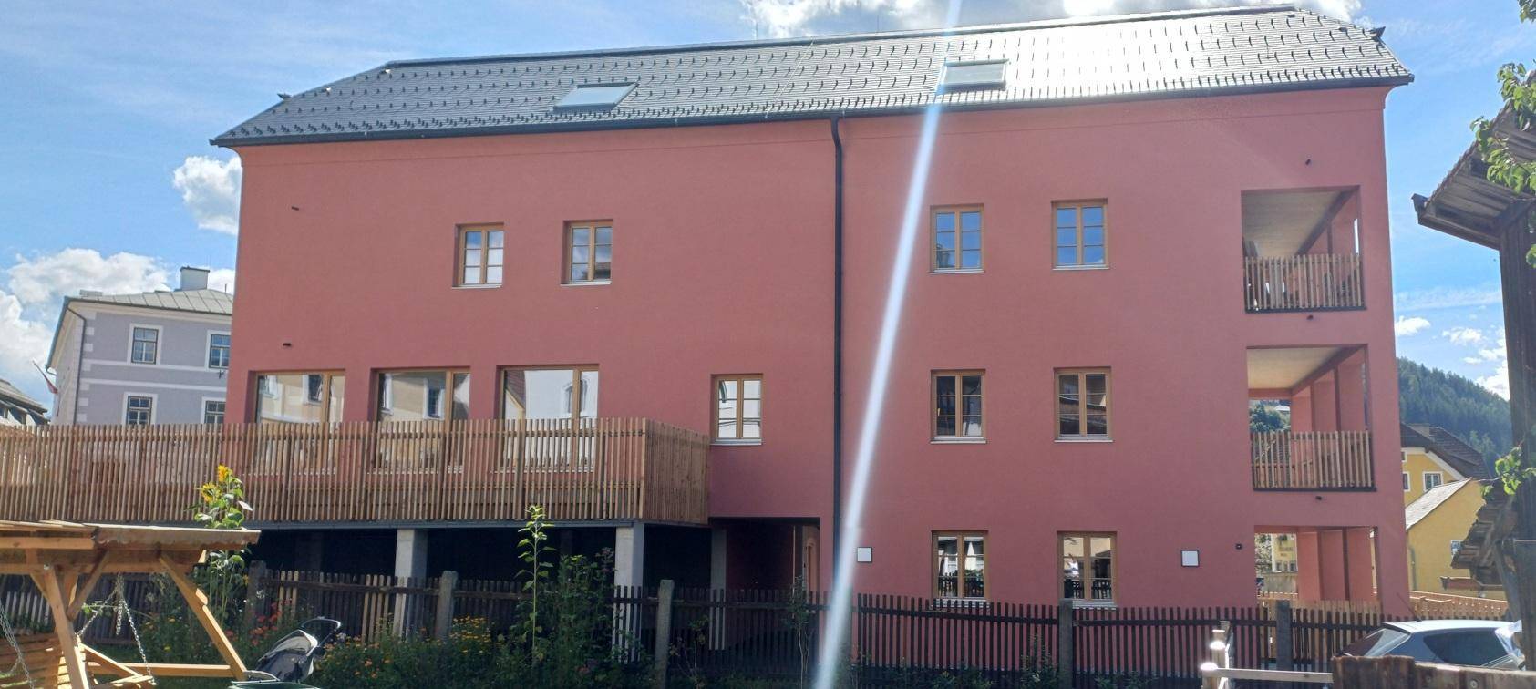 Nahaufnahme der rosafarbenen Gebäudefassade mit zahlreichen Fenstern und Holzgeländern an den Balkonen.