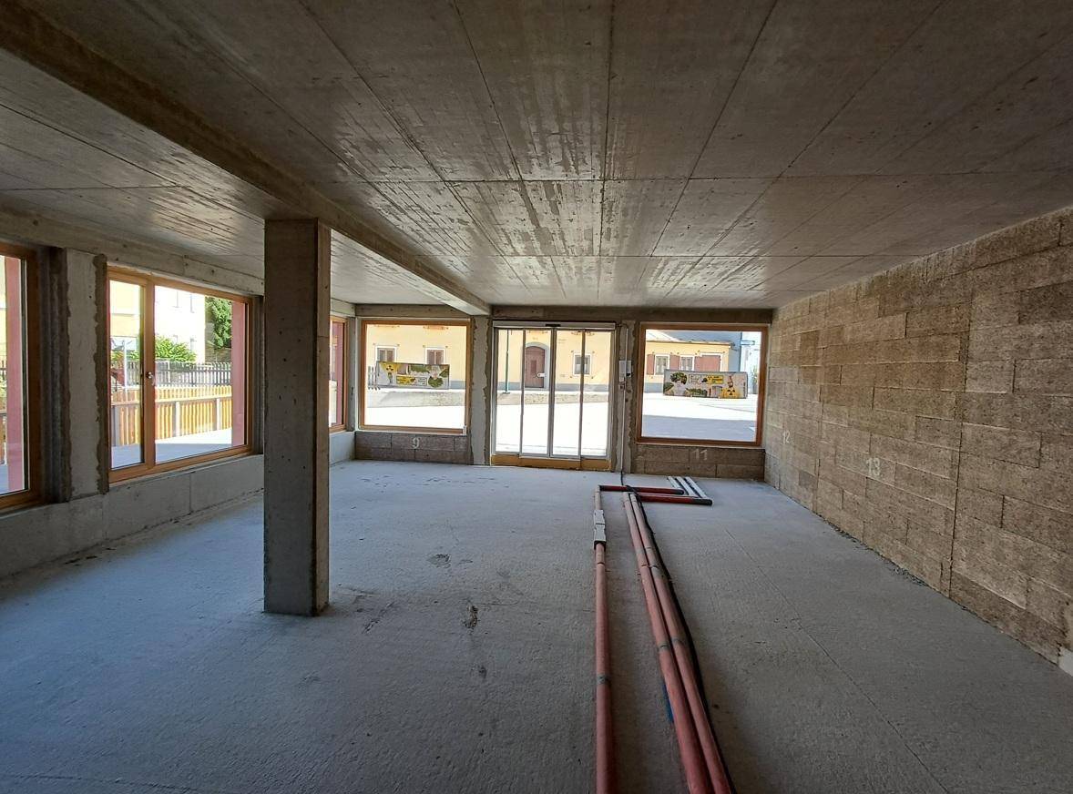 Rohbau-Innenraum mit Betonoberflächen, großen Fenstern und sichtbaren Leitungen, bereit für den Ausbau.