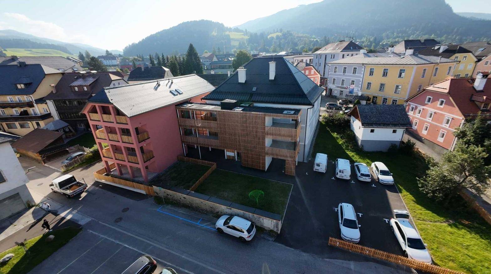 Luftaufnahme des Neubaus und der umliegenden Stadt mit Bergen im Hintergrund und Parkplätzen.