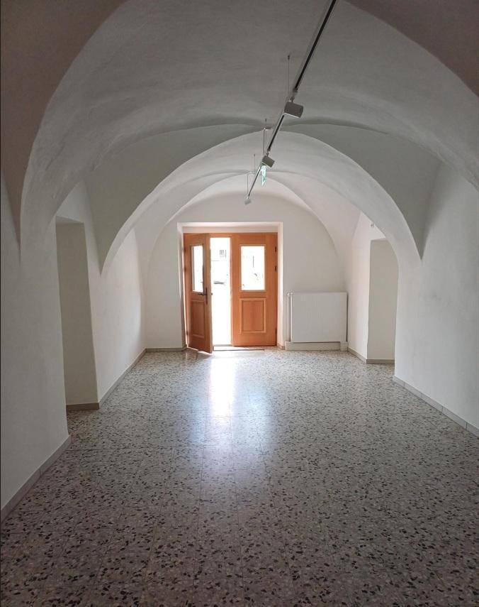 Langer, heller Flur mit gewölbter Decke und Terrazzoboden, der zu einer Holztür mit Tageslicht führt.